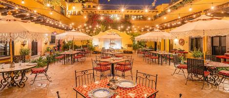 An outdoor dining area with multiple tables and chairs, string lights, and umbrellas.