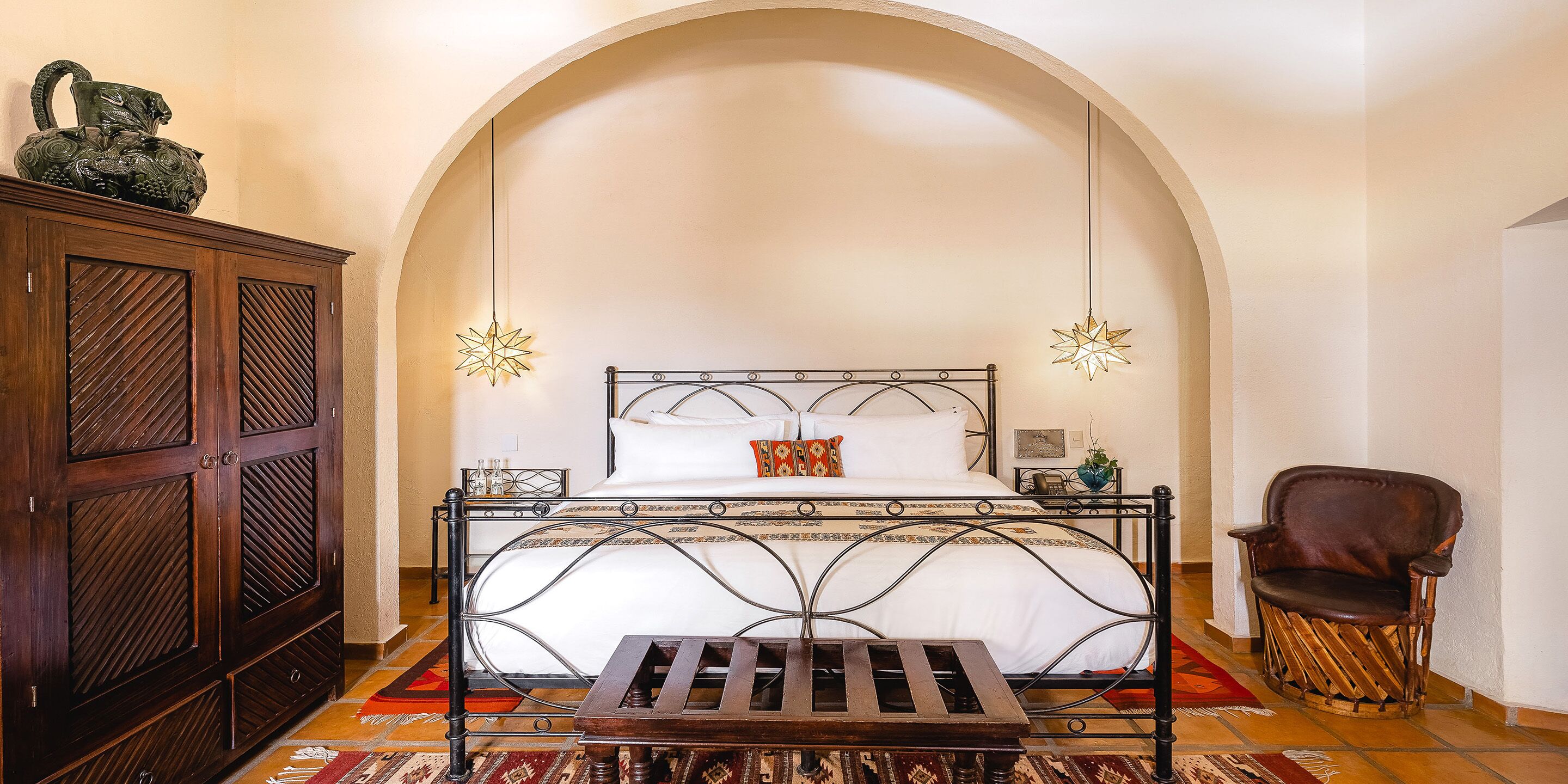 Un dormitorio con una cama, un armario de madera, una silla y una lámpara decorativa colgante.