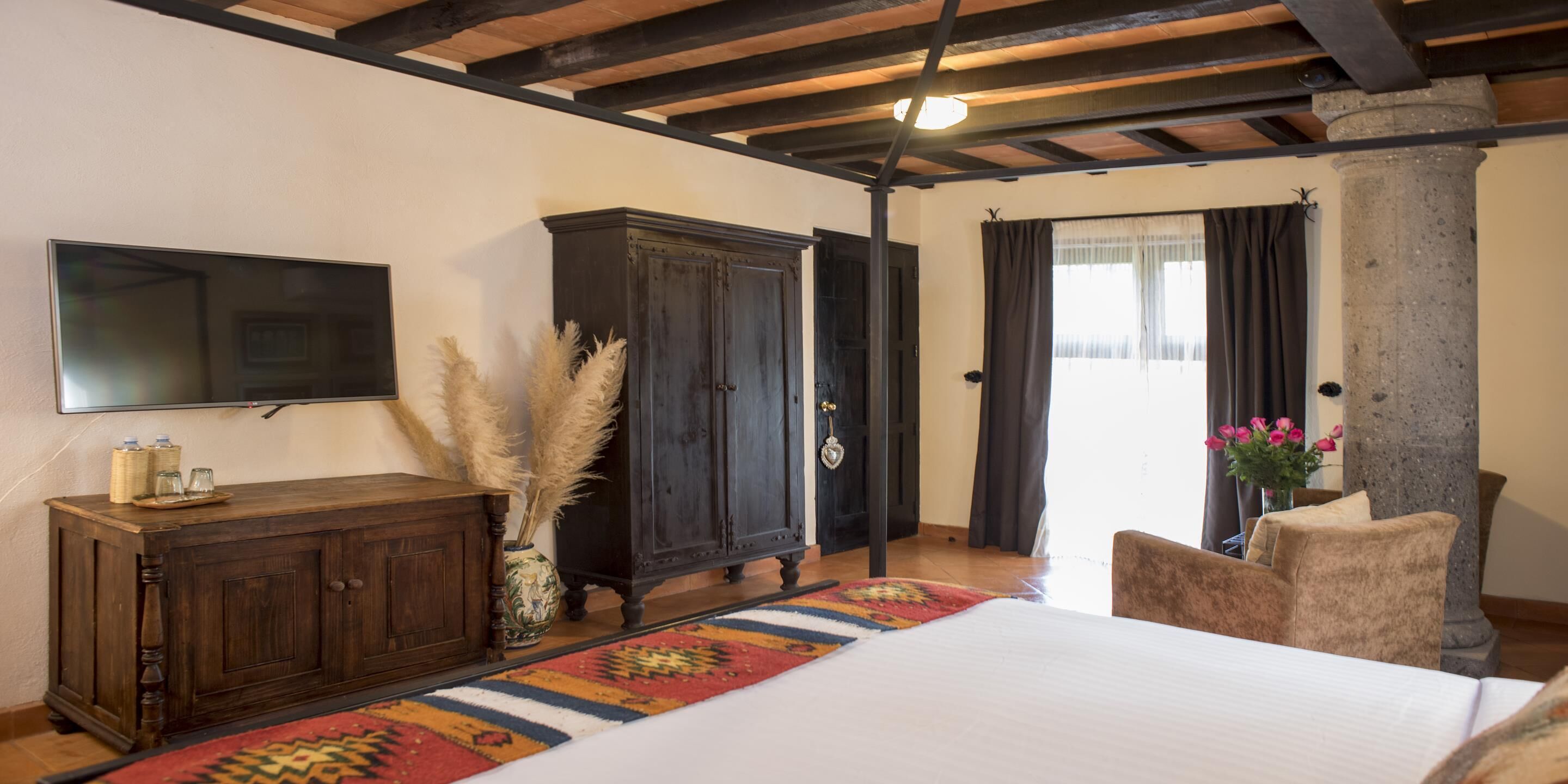 A bedroom with a bed, a wooden cabinet, a television, and a large window with curtains.