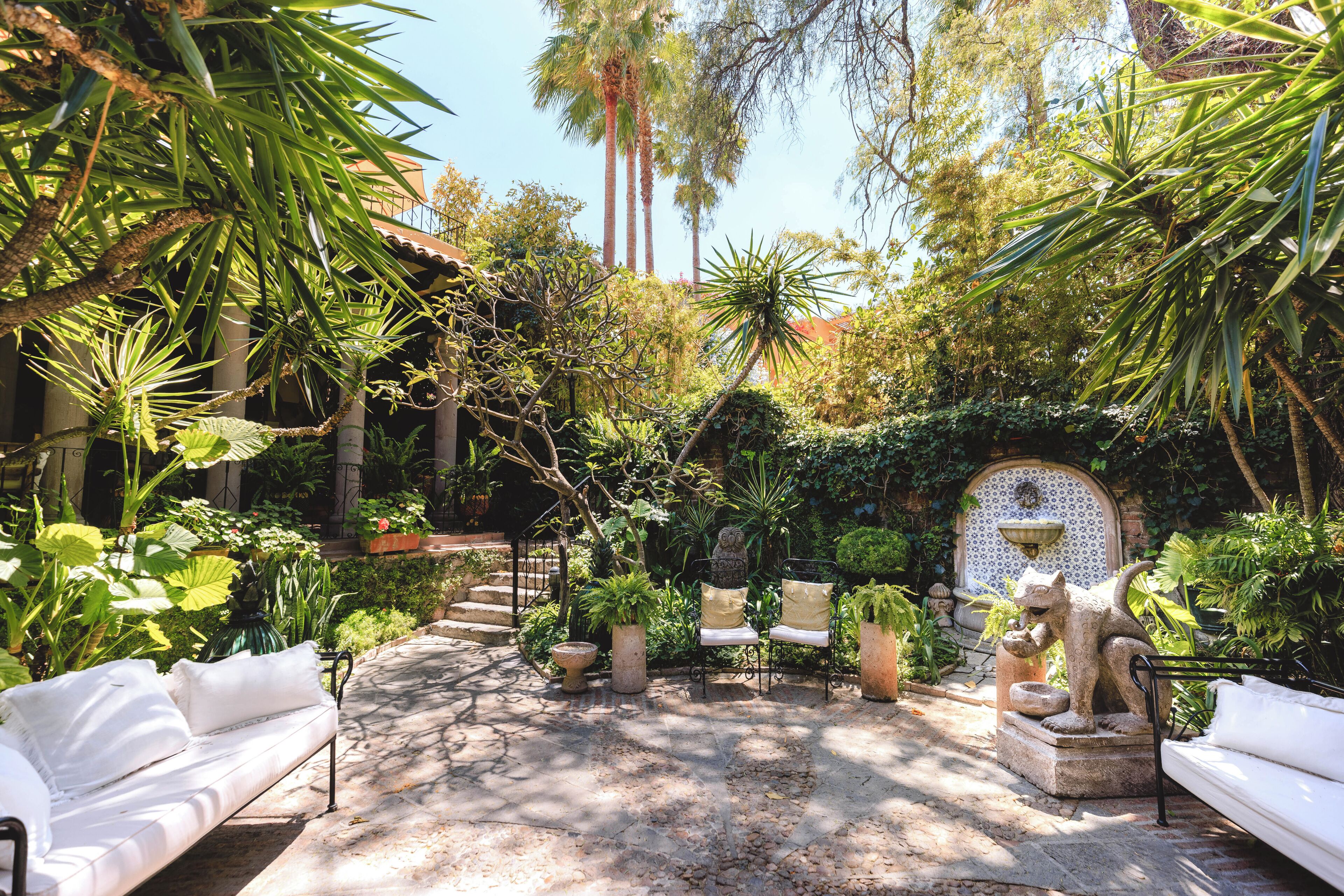 A courtyard with a white sofa, a stone fountain, and various potted plants.