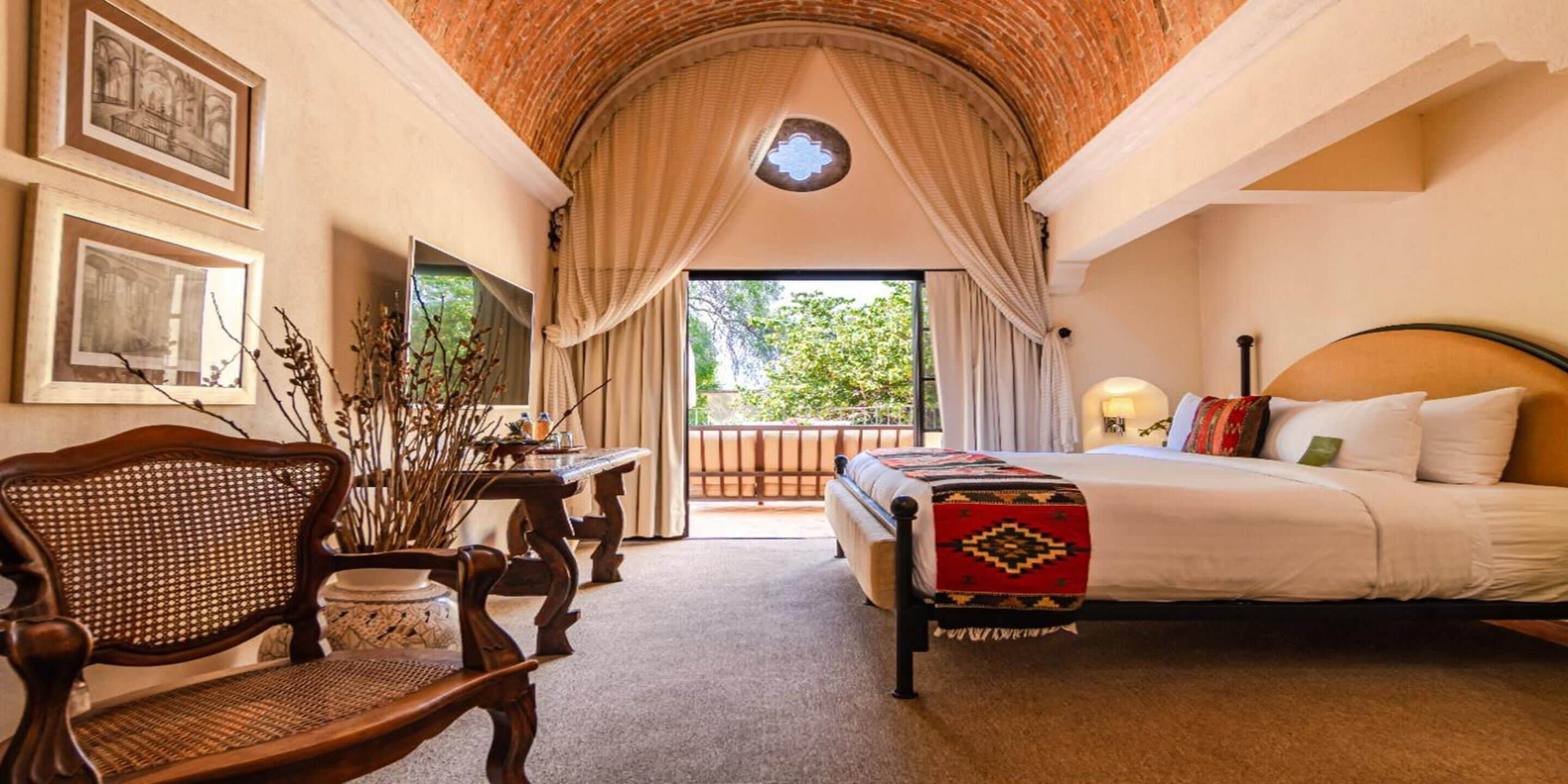 Une chambre à coucher avec un lit, une chaise en bois, une table et une vue sur l’extérieur.