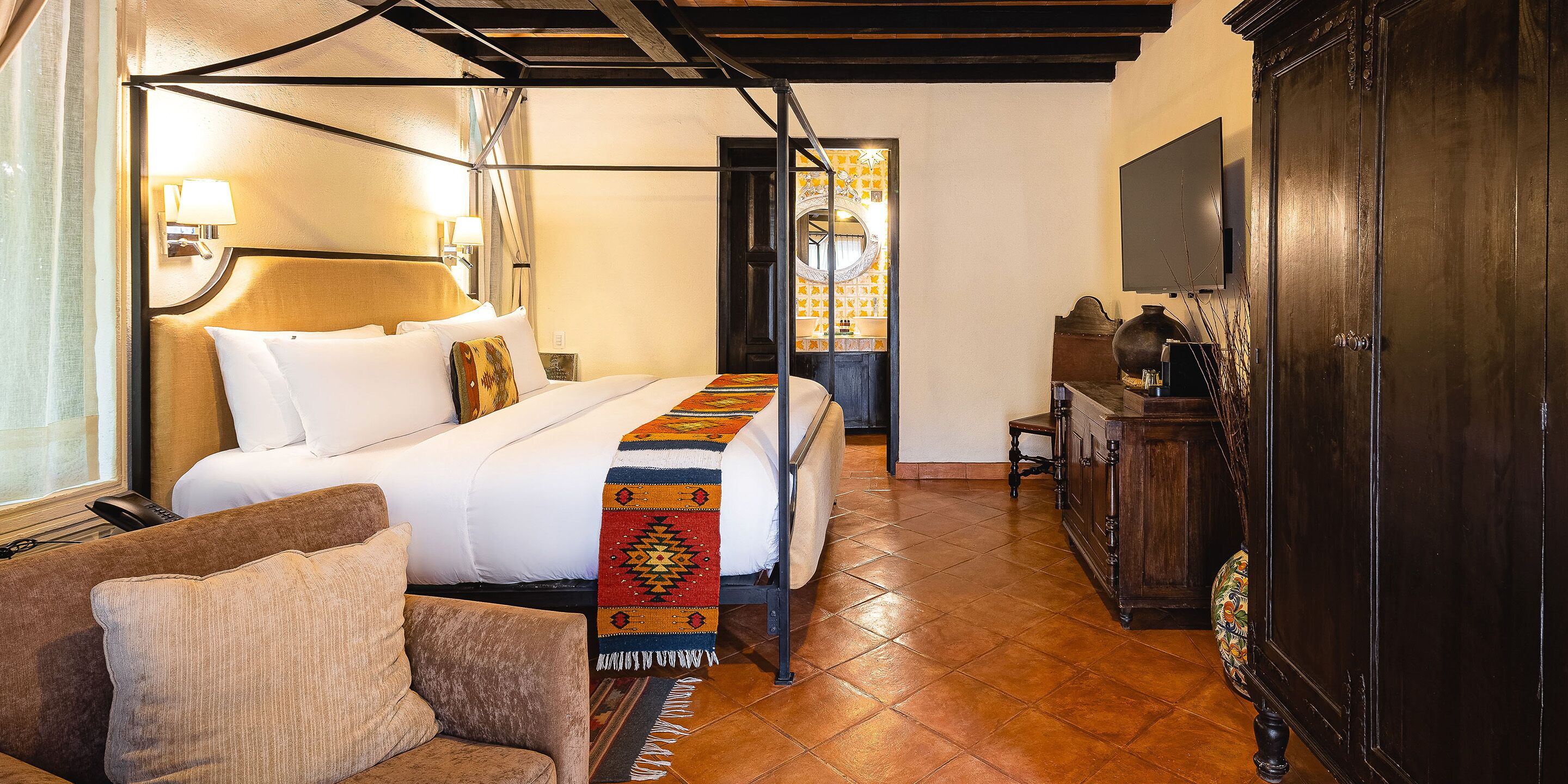 A hotel room with a bed, a sofa, a wooden cabinet, and a TV.