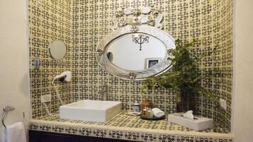 Um banheiro com revestimento de azulejos florais, um espelho redondo, uma pia retangular e uma pequena planta.