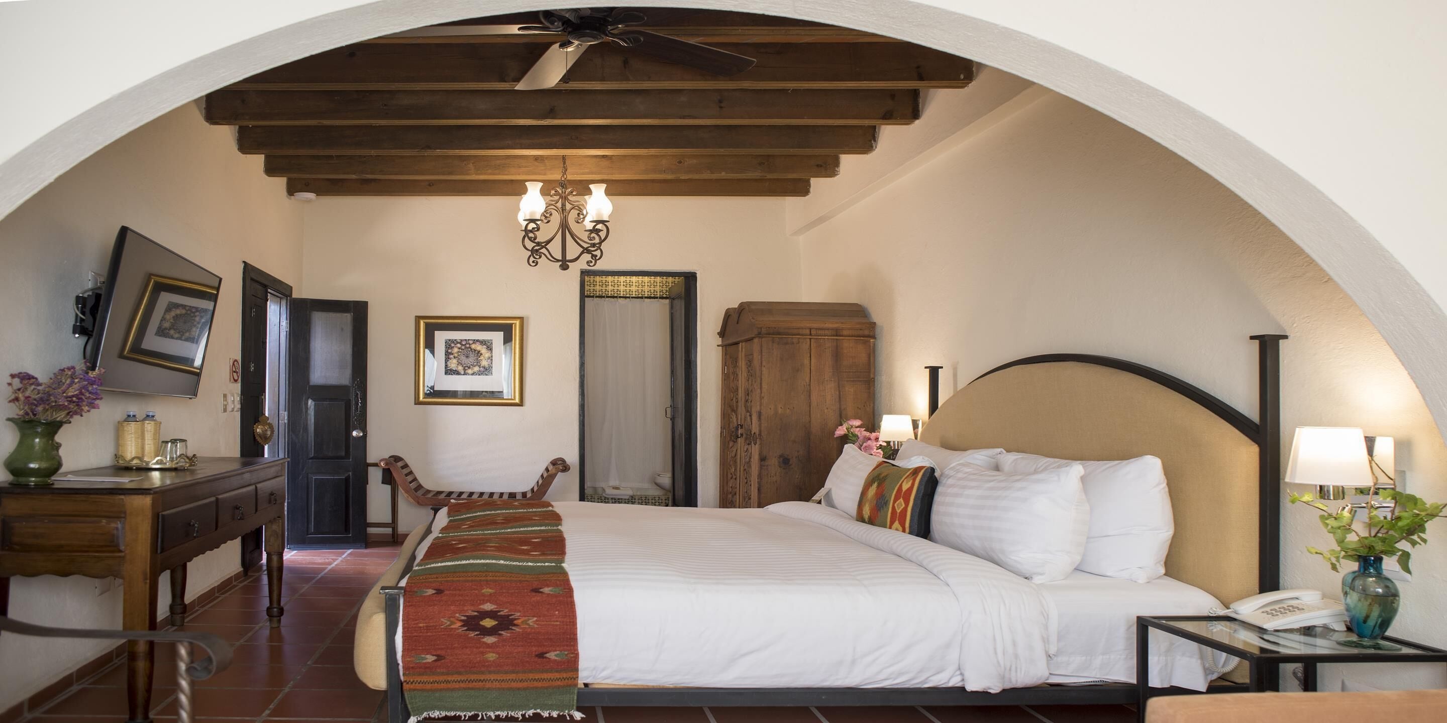 A hotel room with a bed, a desk, a chair, a wardrobe, and a chandelier.