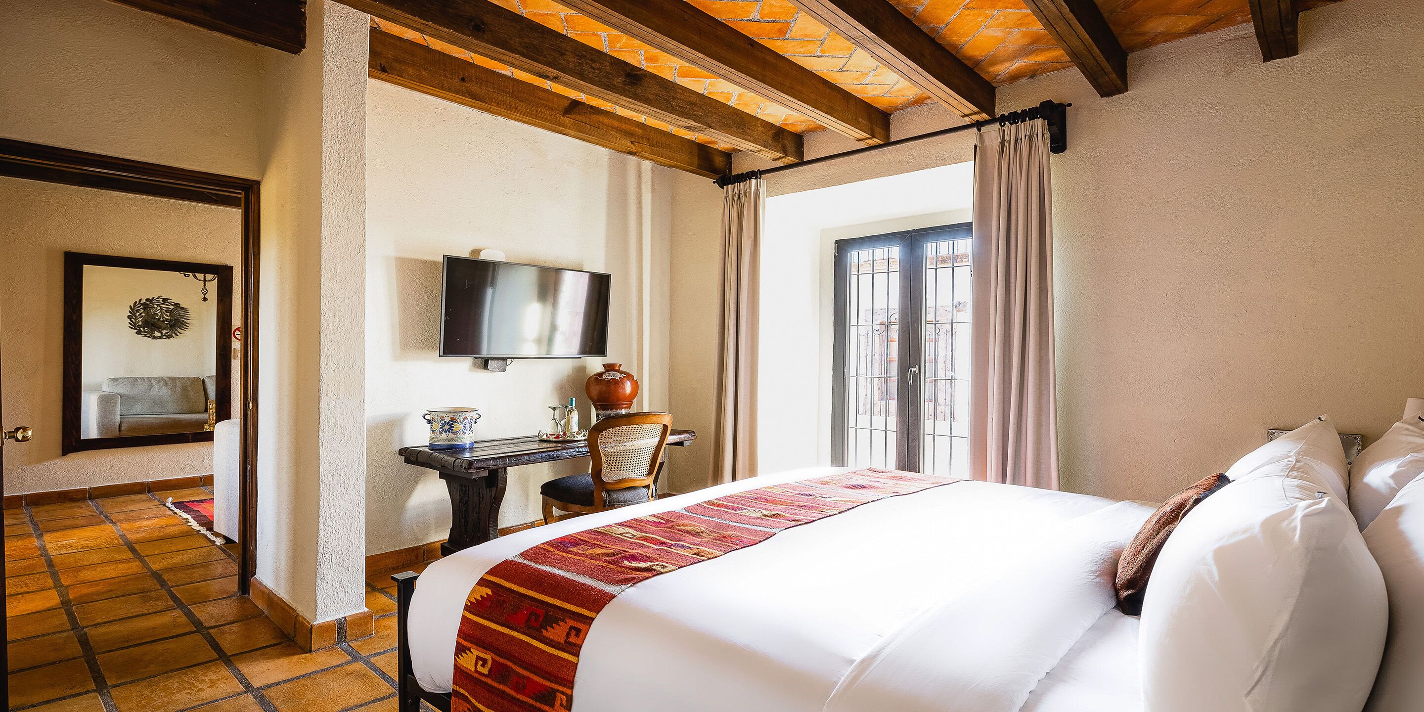 Habitació d'hotel amb llit, televisió, escriptori i cadira, i finestra amb cortines.