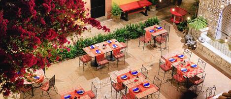 An outdoor patio with multiple tables and chairs, surrounded by potted plants and a red bench.