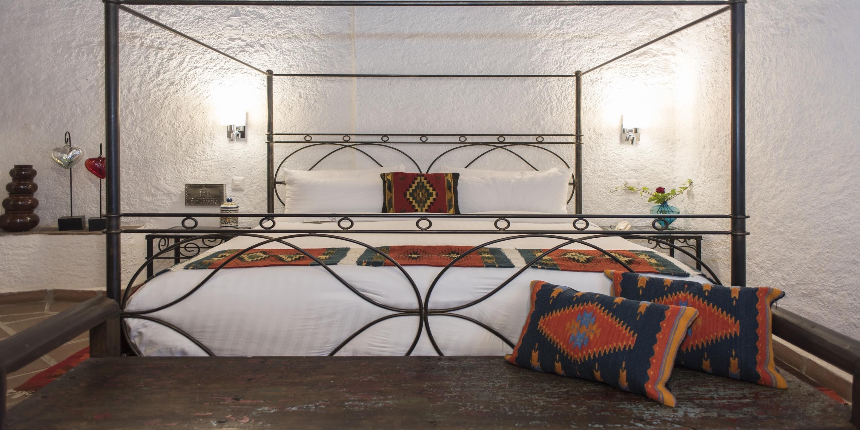 A room with a metal-framed bed, white bedding, and patterned pillows.
