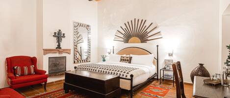 A bedroom with a bed, a red armchair, a wooden coffee table, a patterned rug, and a decorative mirror.
