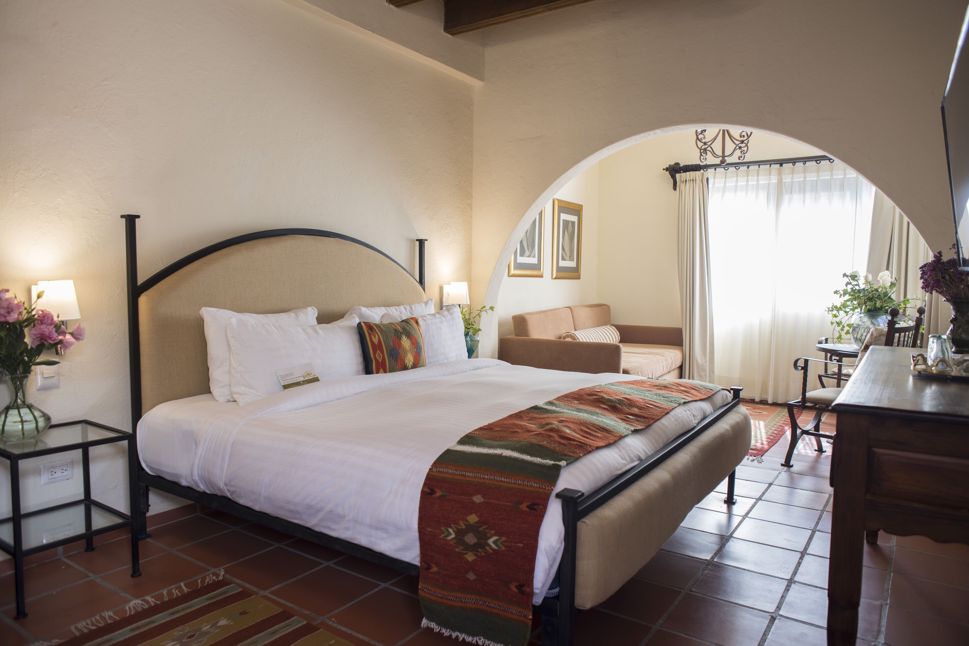 A hotel room with a large bed, a sitting area with a sofa, and a dining table.