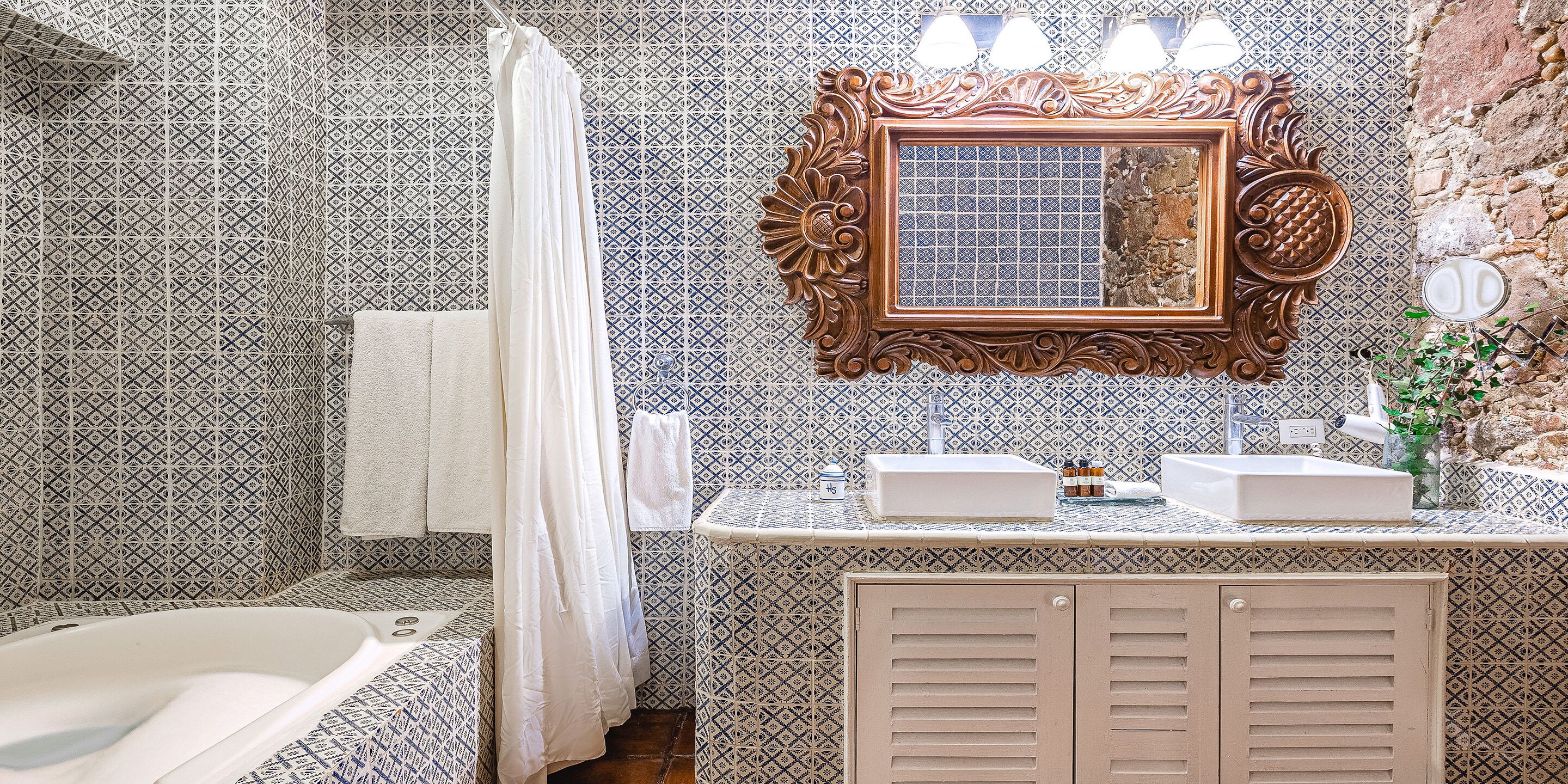 Ein Badezimmer mit Wandfliesen mit Muster, einer Badewanne, einem Waschtisch mit Spiegel und einem Waschbecken mit Pflegeprodukten.