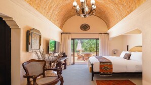 Un dormitorio con una cama grande, una silla de madera, un escritorio con un jarrón y vistas al exterior.