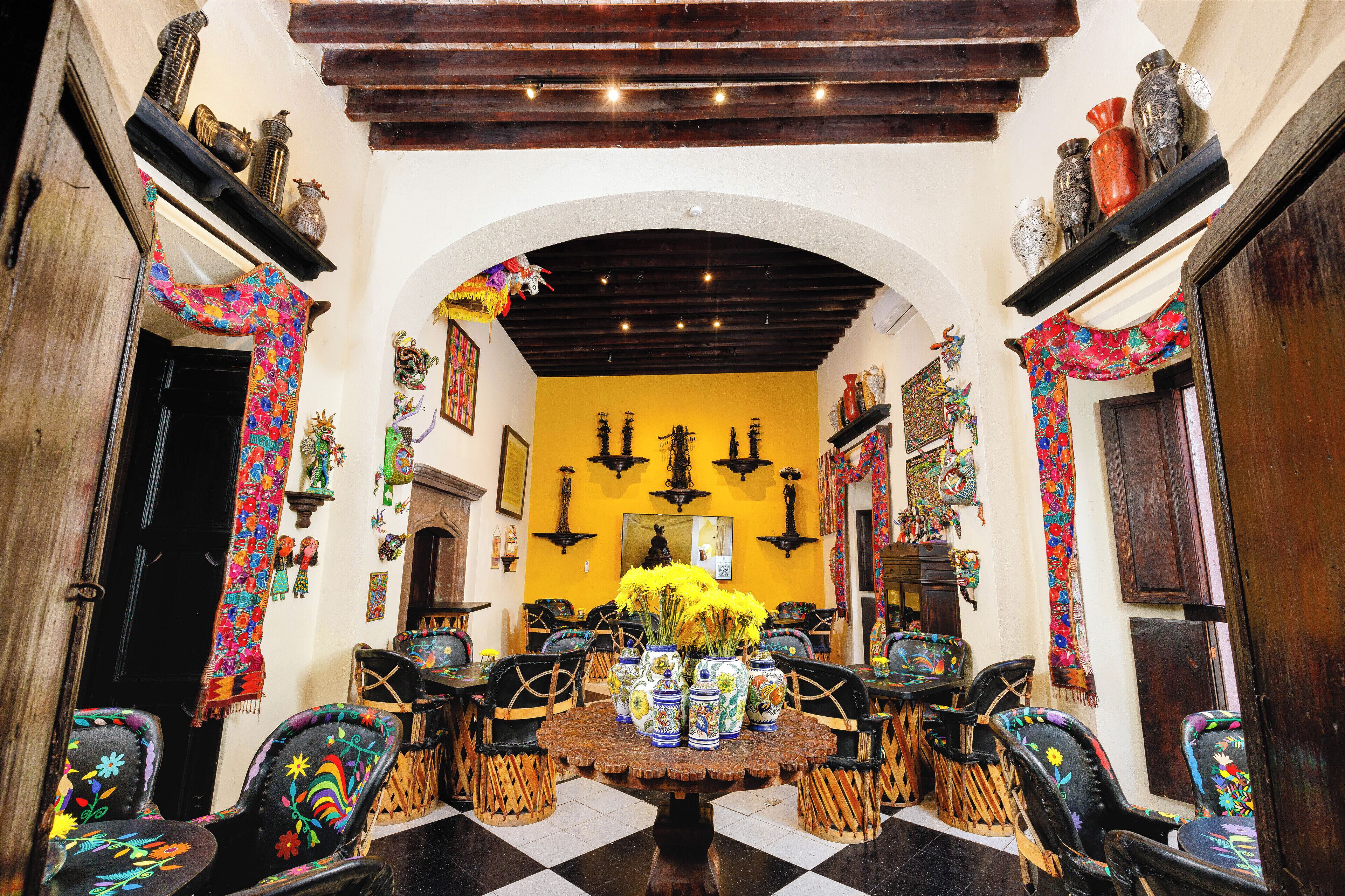 Un comedor con una mesa redonda central rodeada de sillas, una pared amarilla y elementos decorativos.