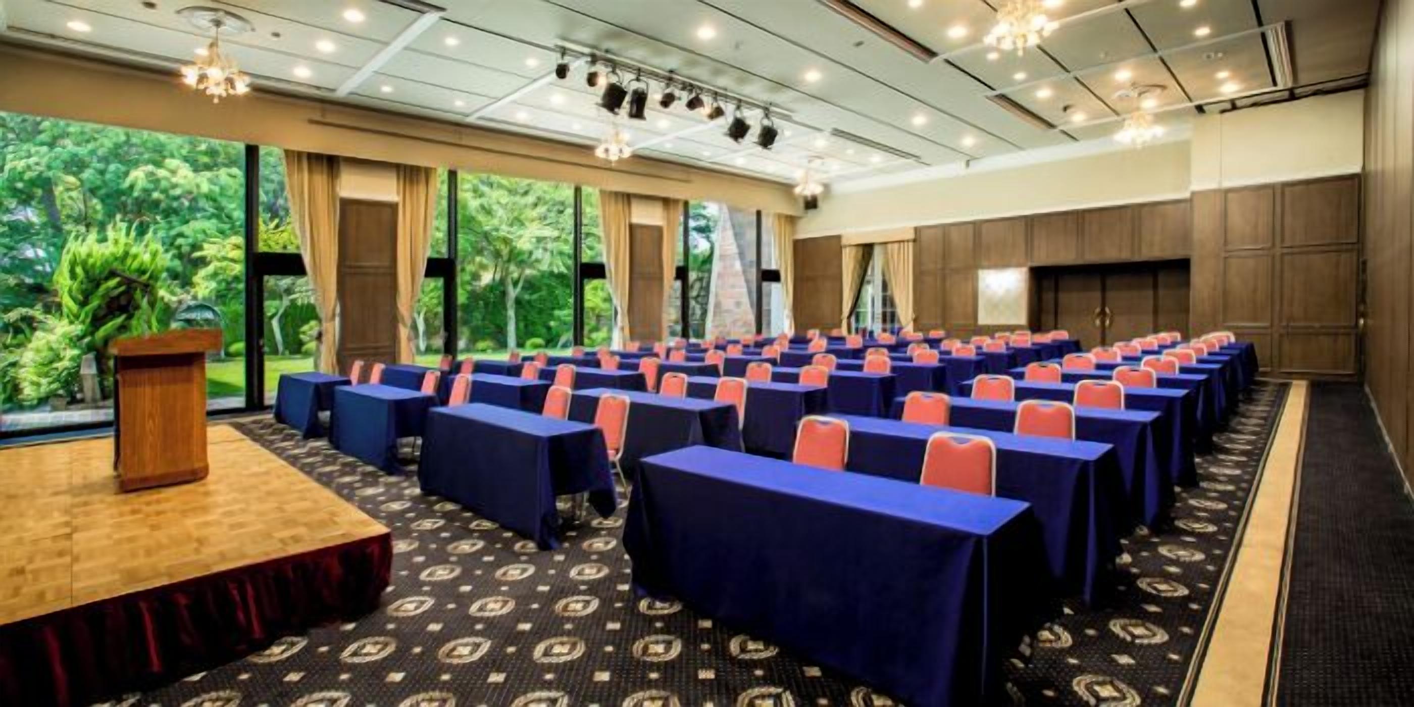 A conference room with rows of tables, a podium, and large windows overlooking greenery.