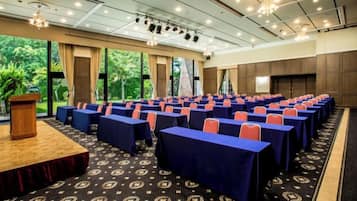 A conference room with rows of tables, a podium, and large windows overlooking greenery.