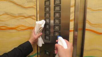 Una persona limpiando un panel de control de ascensor con un paño y un rociador.