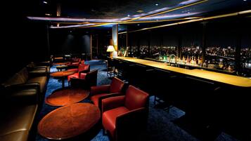 A bar area with leather seating, a long counter with bottles, and a city view through large windows.