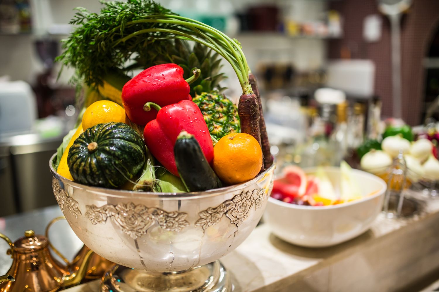 Un tazón de verduras frescas, como pimientos, calabacín y zanahorias, sobre una mesa con una tetera decorativa cerca.