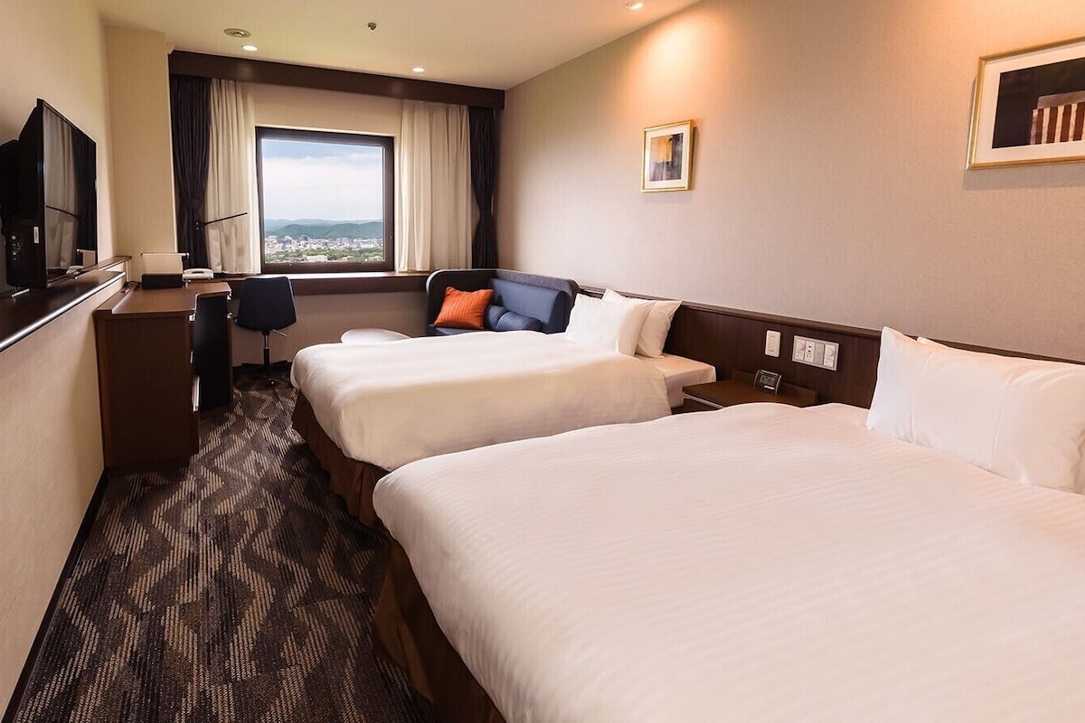 Een hotelkamer met twee bedden, een bureau met stoel, een televisie en een raam met uitzicht.