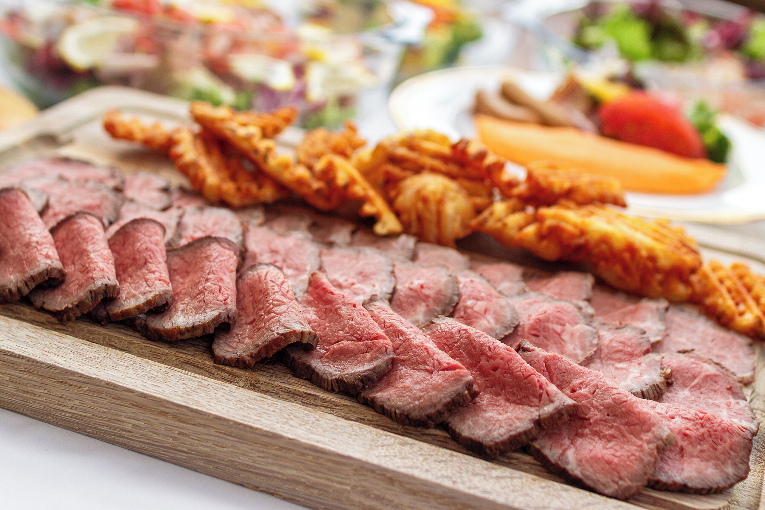A wooden cutting board with sliced meat and fried items.