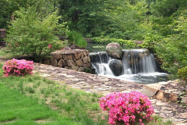 A waterfall cascading over rocks, surrounded by lush greenery and pink flowering bushes. - Okayama International Hotel (Okayama)
