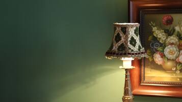 A table with a decorative lamp, a tissue box, and a small container, against a green wall with a framed floral painting.