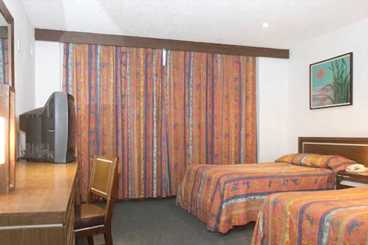 A hotel room with two beds, a desk with a chair, a television, and a painting on the wall.