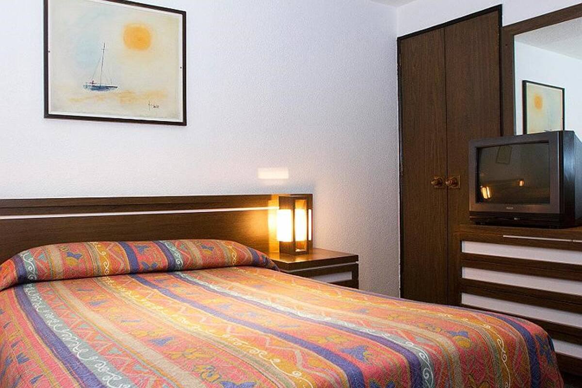 A hotel room with a bed, a nightstand with a lamp, a television, and a door.