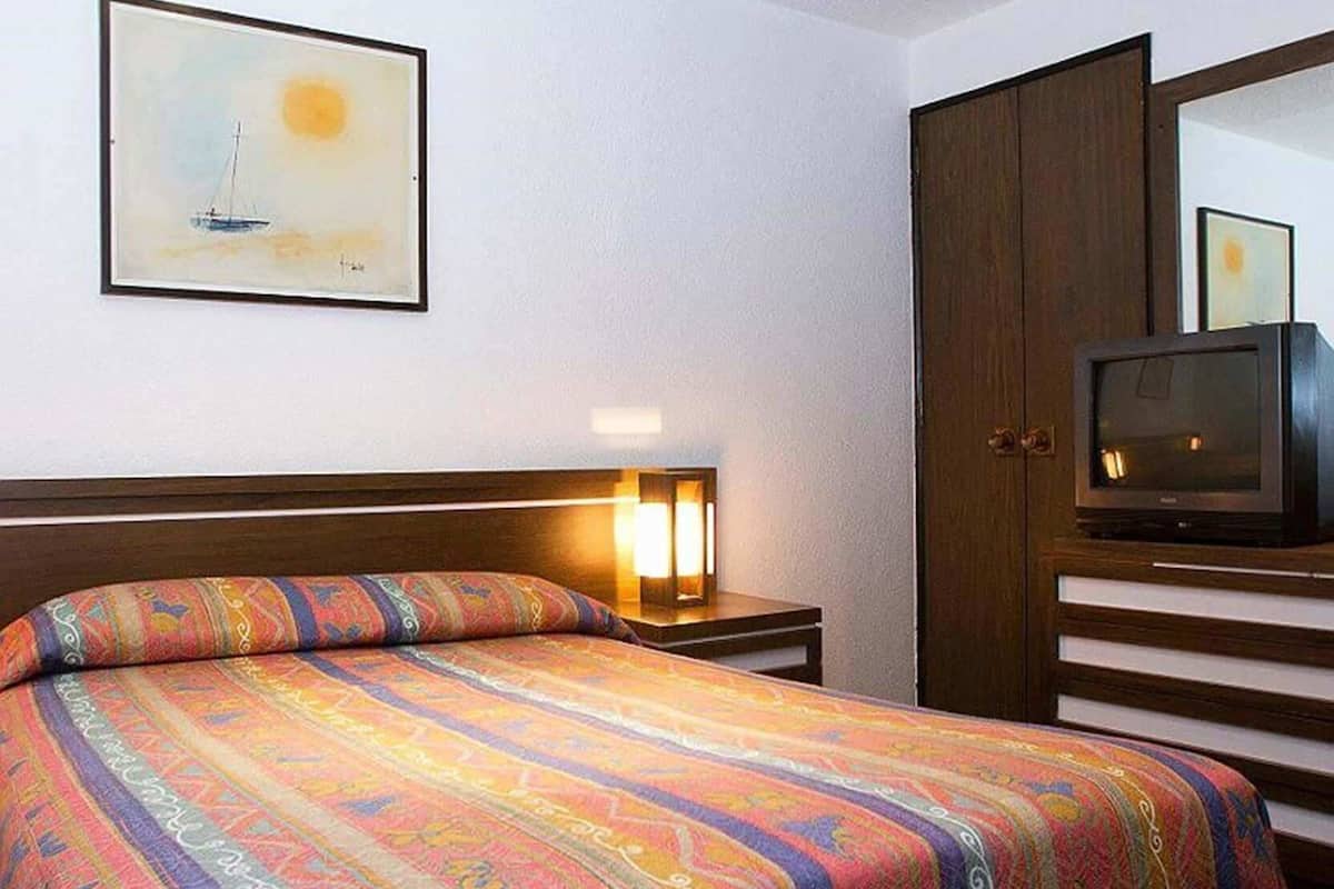 A hotel room with a bed, a nightstand, a TV, a wardrobe, and a painting on the wall.