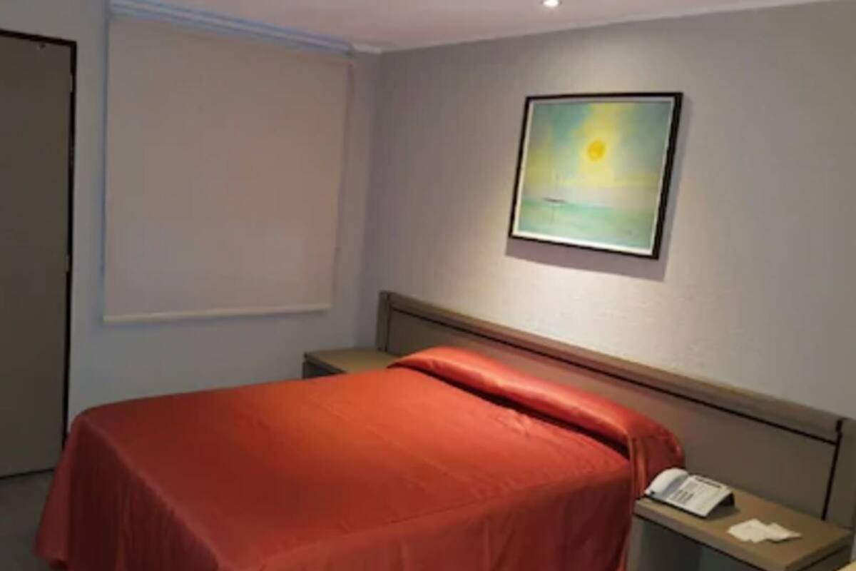 A hotel room with a bed, a nightstand, a telephone, and a painting on the wall.