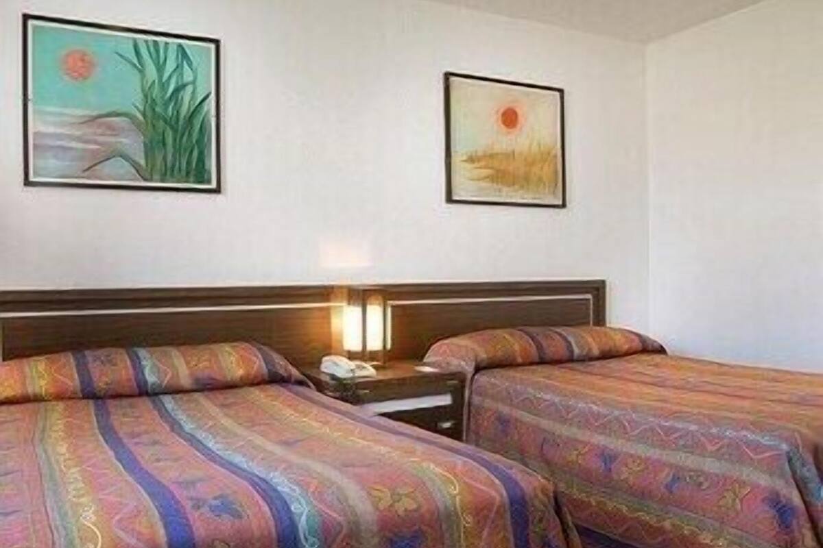 A hotel room with two beds, a nightstand, and two wall-mounted paintings.