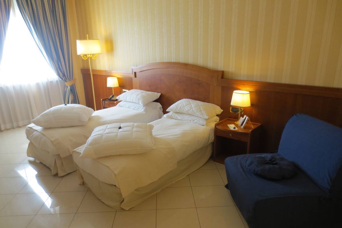 A hotel room with two beds, a blue sofa, and two bedside lamps.