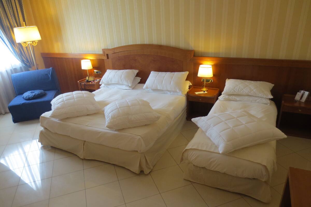 A hotel room with two beds, a blue armchair, and bedside lamps.