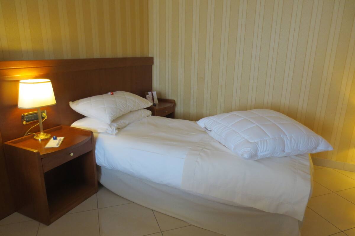 A hotel room with a bed, a nightstand with a lamp, and a wall with vertical stripes.