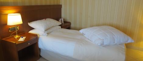 A hotel room with a bed, a nightstand with a lamp, and a wall with vertical stripes.