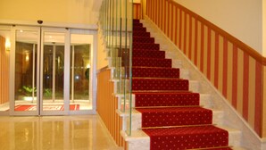 Una escalera con peldaños alfombrados en rojo y barandillas de vidrio, que conduce a un cuarto con alfombra roja y una puerta de cristal.