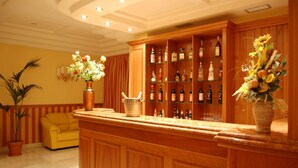 Una zona de bar con armarios de madera y una barra, un sofá amarillo y plantas en macetas.