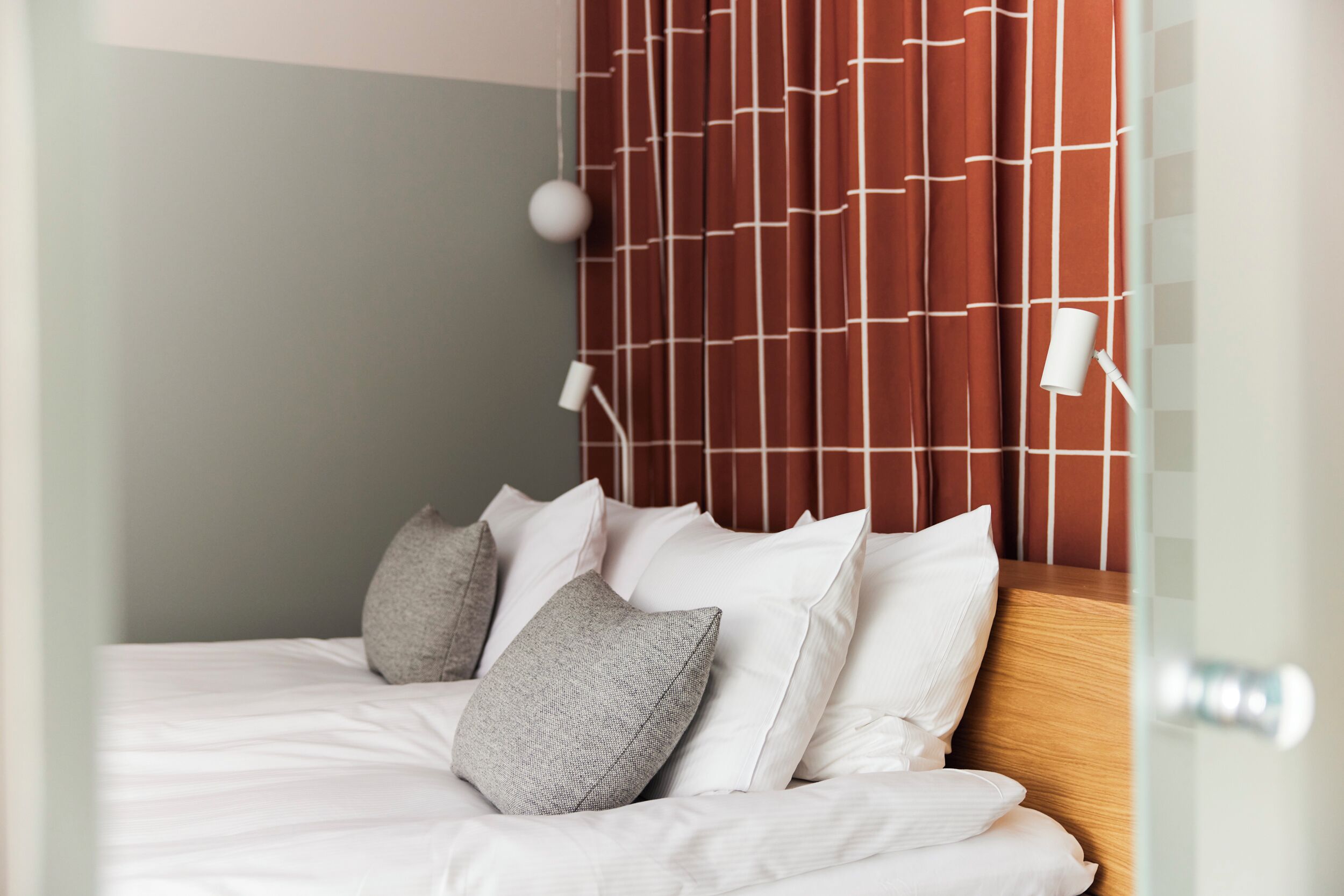 A neatly made bed with white linens and multiple pillows, a wooden headboard with a geometric pattern, and a bedside lamp.