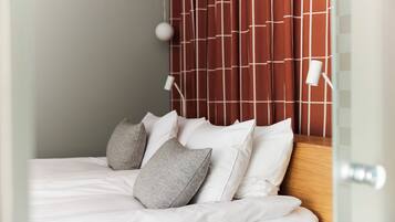 A neatly made bed with white linens and multiple pillows, a wooden headboard with a geometric pattern, and a bedside lamp.