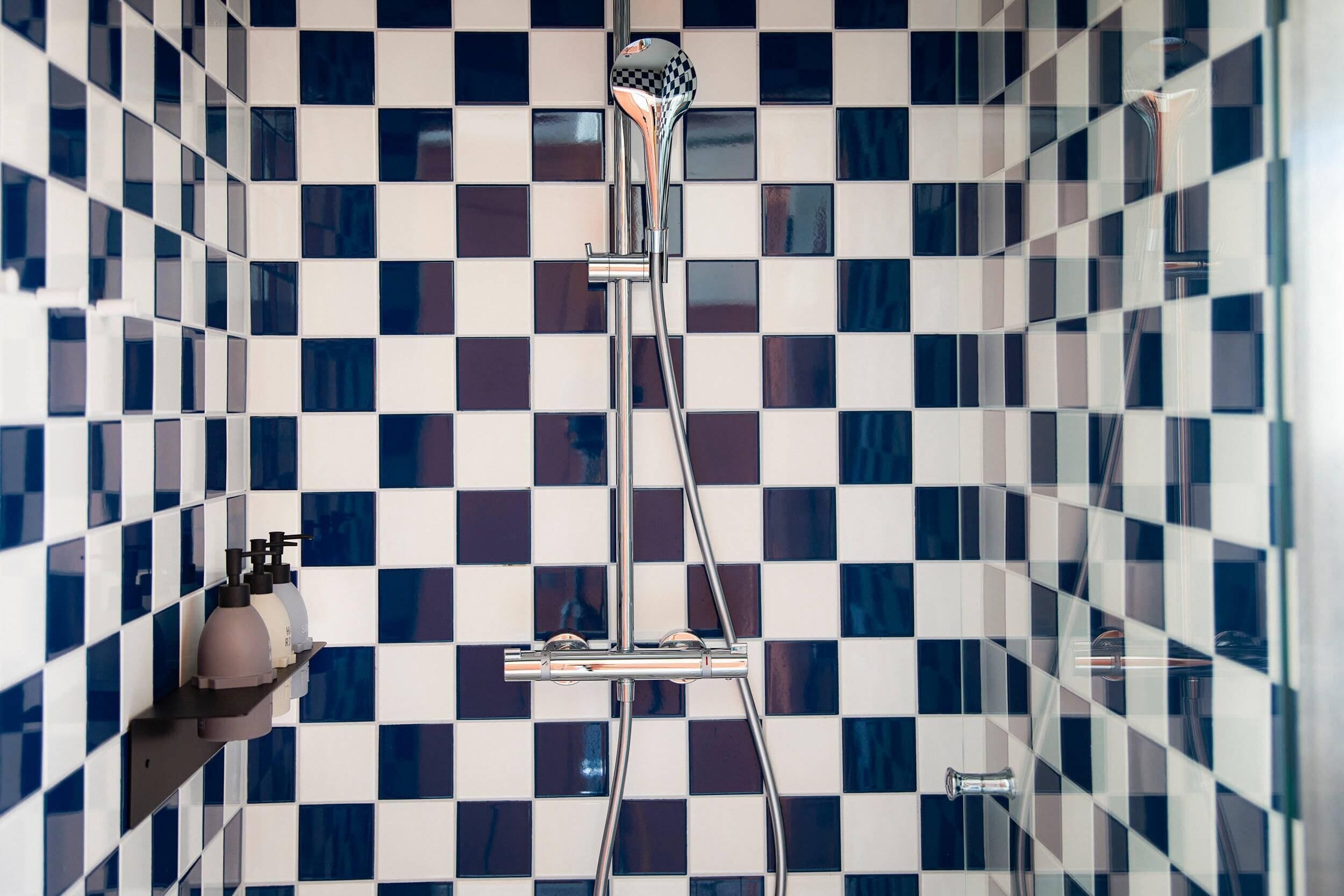 Un baño con pared de baldosas a cuadros, cabezal de ducha y dispensador de jabón.