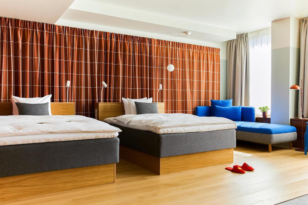 A modern hotel room with two beds, a sofa, and a large window.