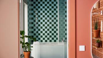 A bathroom with a checkered tile wall, a bathtub, and potted plants.