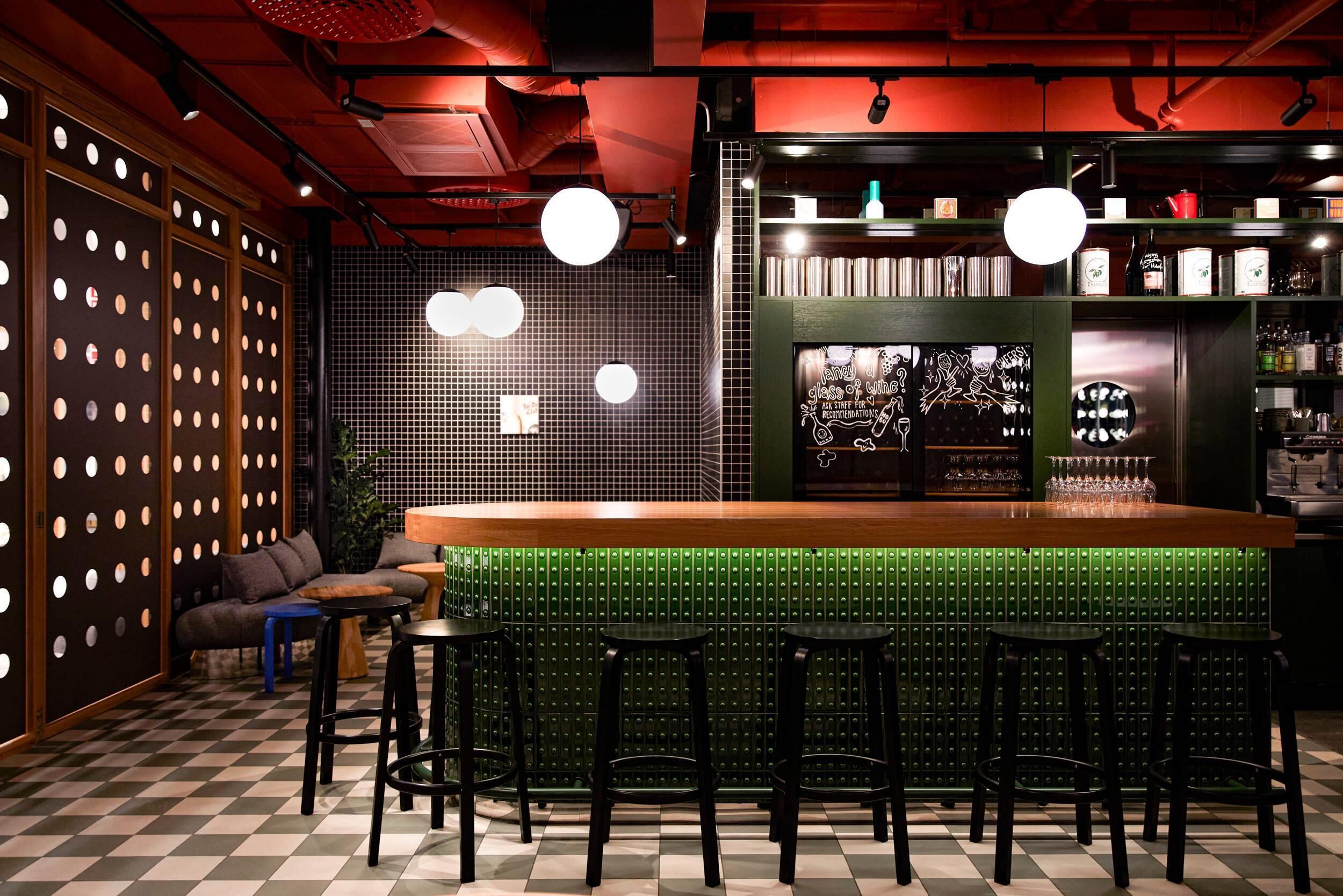 Zona de bar con taburetes, piso a cuadros y pared verde con diseño de cuadrícula.