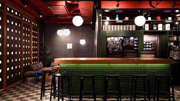 Zona de bar con taburetes, piso a cuadros y pared verde con diseño de cuadrícula.