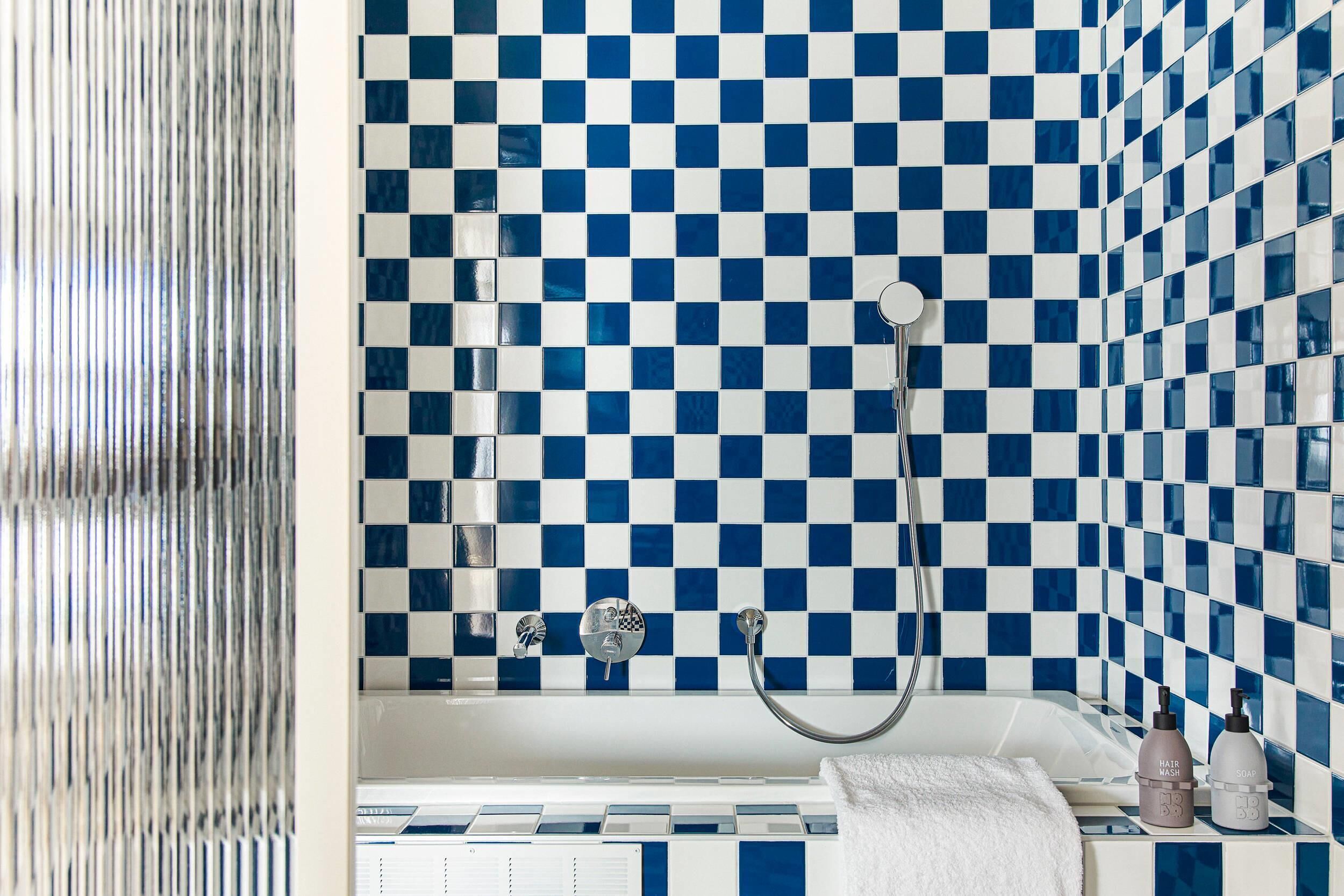 A bathroom with a checkered blue and white tile wall, a white bathtub, and a white towel on the edge.