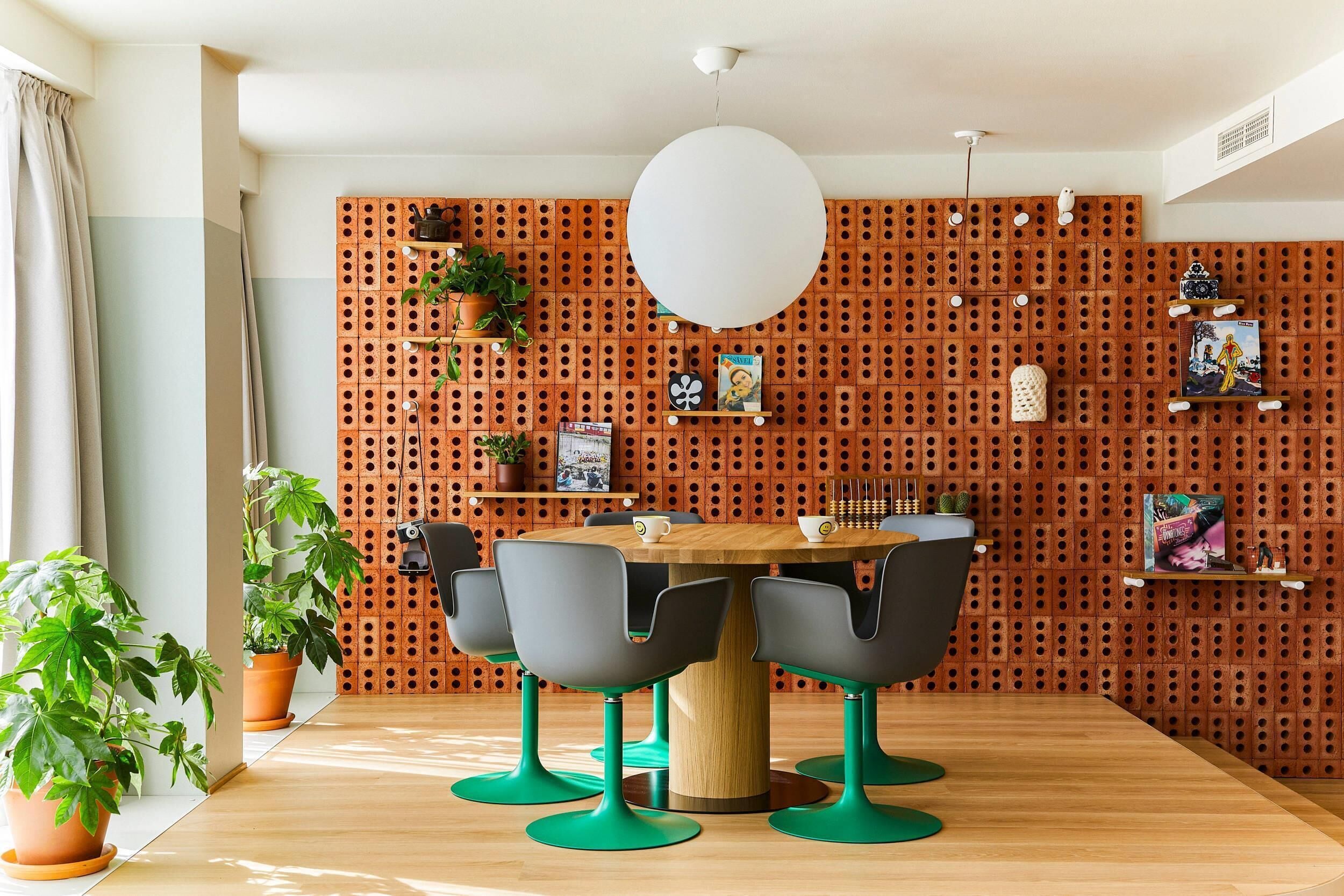 A modern dining area with a wooden table, four chairs, and a brick-patterned wall with shelves.