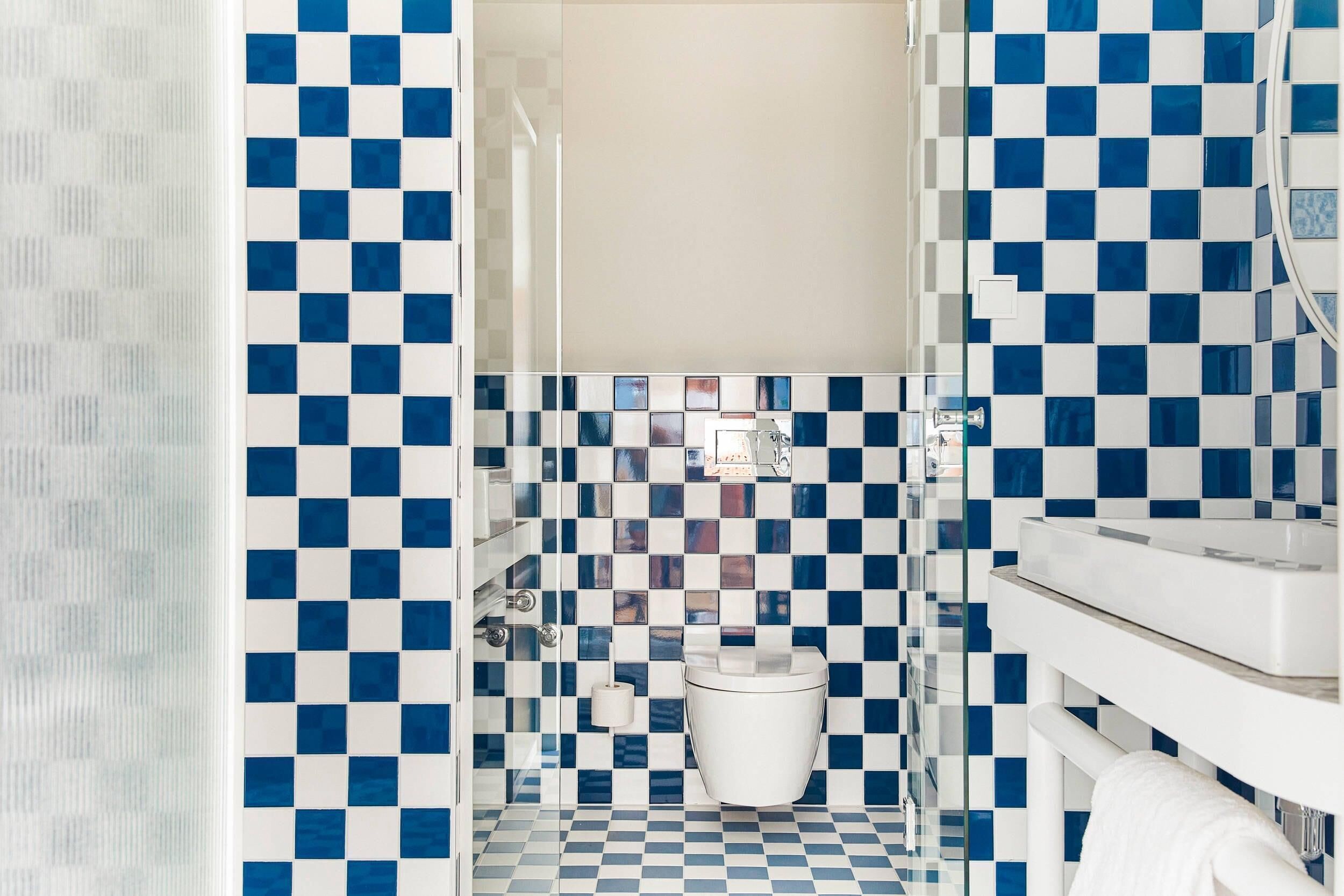 Ein Badezimmer mit Schachbrettfliesen, einer weißen Toilette und einer Duschkabine aus Glas.