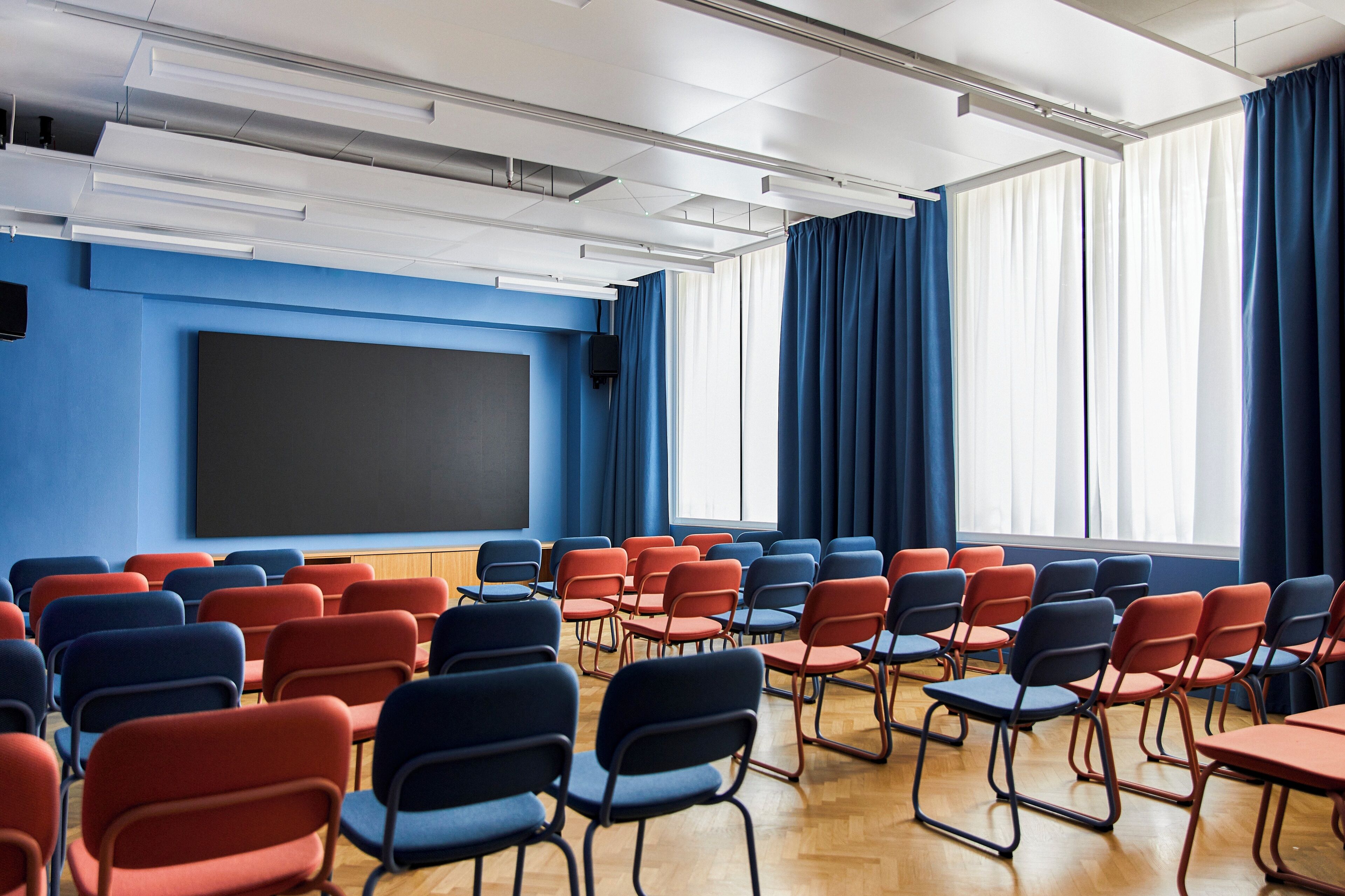 Un'aula con file di sedie, una lavagna e ampie finestre con tende blu.