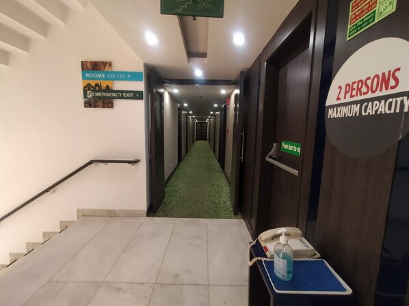 A hotel hallway with signs indicating room numbers 103-110, an emergency exit, and a 2-person capacity sign.