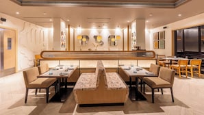 A modern restaurant with a central booth seating, tables with chairs, and decorative wall art. - Park Inn by Radisson New Delhi Lajpat Nagar (New Delhi)