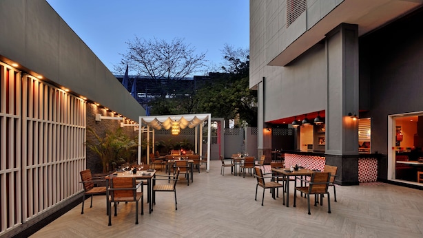 An outdoor dining area with multiple tables and chairs, a pergola with string lights, and a restaurant visible through an open doorway. - Park Inn by Radisson New Delhi Lajpat Nagar (New Delhi)